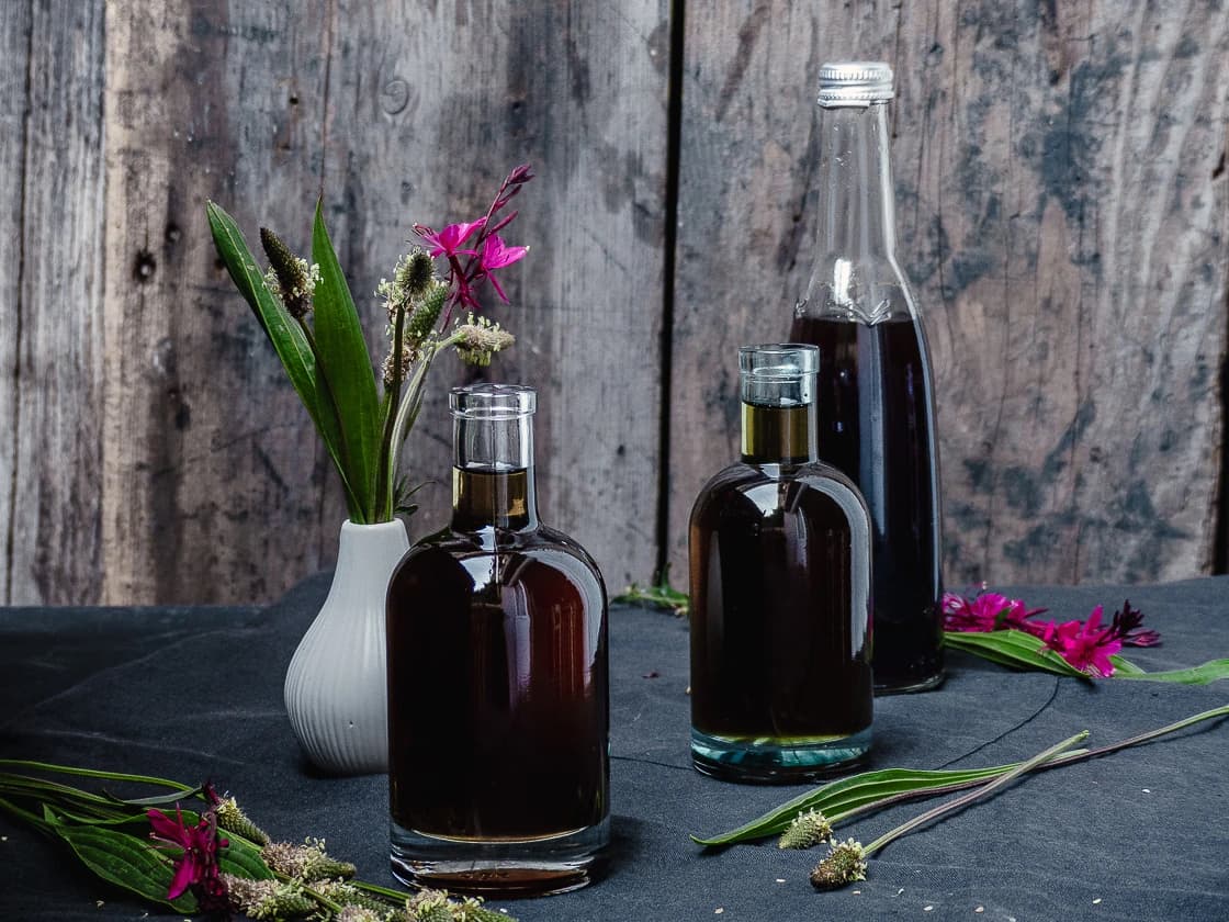 3 flacons de sirop de plantain avec un petit vase blanc contenant des feuilles de plantain